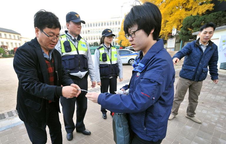 An official checks a certificate of a South Korean student before students take the College Scholastic Ability Test, a standardised exam for college entrance, at a gate of a high school in Seoul, on November 7, 2013