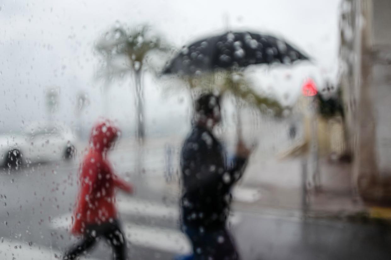 A person holding an umbrella and another walk behind a wet window in the French Riviera city of Nice, southern France on April 19, 2020. (Photo by VALERY HACHE / AFP) (Photo by VALERY HACHE/AFP via Getty Images)