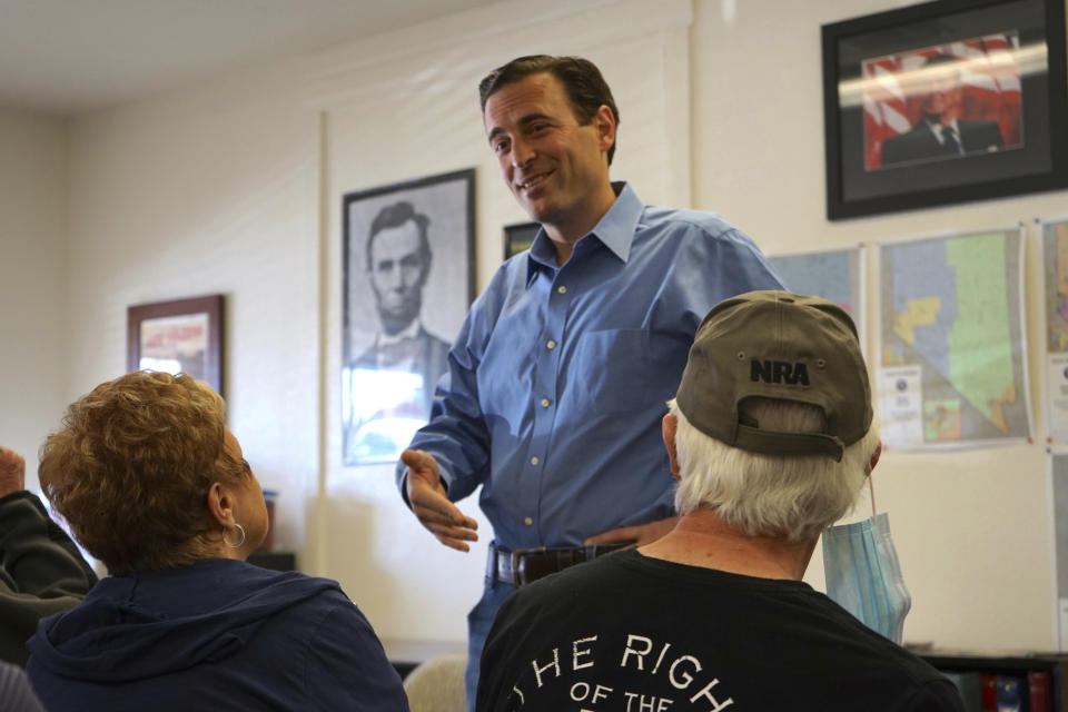 In this Sunday, Oct. 10, 2021, photo Republican Adam Laxalt, flanked by pictures of Presidents Abraham Lincoln and Ronald Reagan, talks to a supporter at the Douglas County Republican Party Headquarters on the final day of his Senate campaign's statewide tour in Gardnerville, Nev. Republican Laxalt hopes to win the race for Nevada's U.S. Senate seat by drawing stark between his positions and the direction he says Democrats and their allies in Big Tech, Hollywood and the media are taking the country. (AP Photo/Sam Metz)