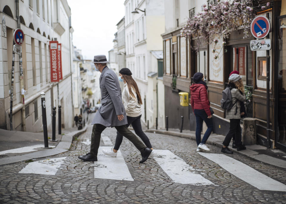 People wearing face masks walk, in the Montmartre district of Paris, Sunday Oct. 25, 2020. A curfew intended to curb the spiraling spread of the coronavirus, has been imposed in many regions of France including Paris and its suburbs. (AP Photo/Lewis Joly)