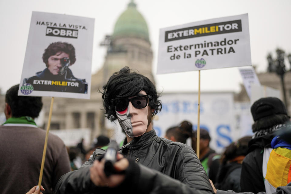 A masked anti-government protester aims a toy gun during a demonstration outside Congress where lawmakers debate a reform bill promoted by President Javier Milei in Buenos Aires, Argentina, Wednesday, June 12, 2024. The sign at right reads in Spanish "Exterminator of the homeland." (AP Photo/Natacha Pisarenko)