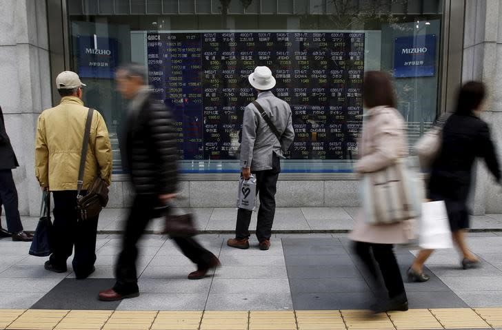 Pedestrians look at an electronic board showing the various stock prices outside a brokerage in Tokyo April 9, 2015. REUTERS/Yuya Shino/Files