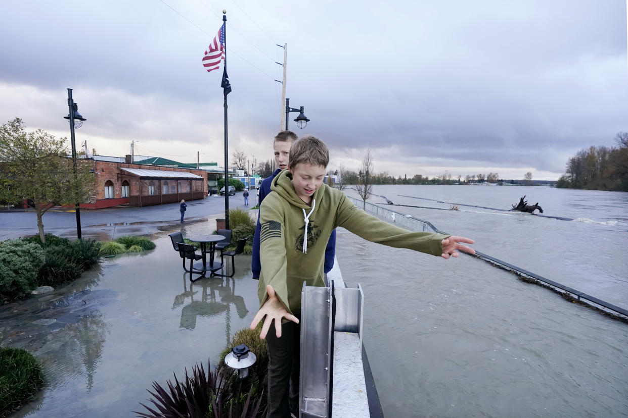 Two boys balance atop a flood wall holding back the flooded Skagit River, right, in downtown Mount Vernon, Wash., Tuesday, Nov. 16, 2021. An atmospheric river—a huge plume of moisture extending over the Pacific and into Washington and Oregon—caused heavy rainfall in recent days, bringing major flooding in the area. (AP Photo/Elaine Thompson)