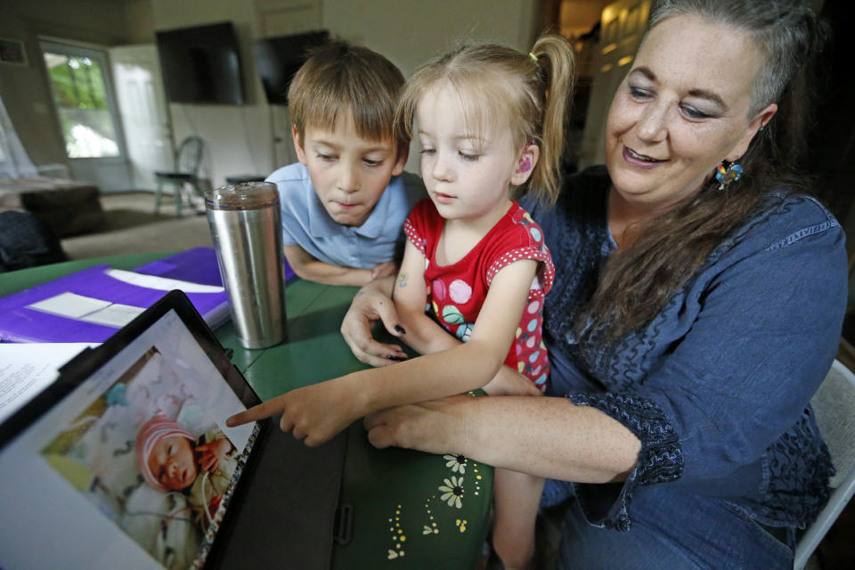 In this Thursday, June 6, 2019, photo, Victory points to her baby photo, as her brother Richard and her mother Amie Schofield look on, at their home in Ogden, Utah. (AP Photo/Rick Bowmer)