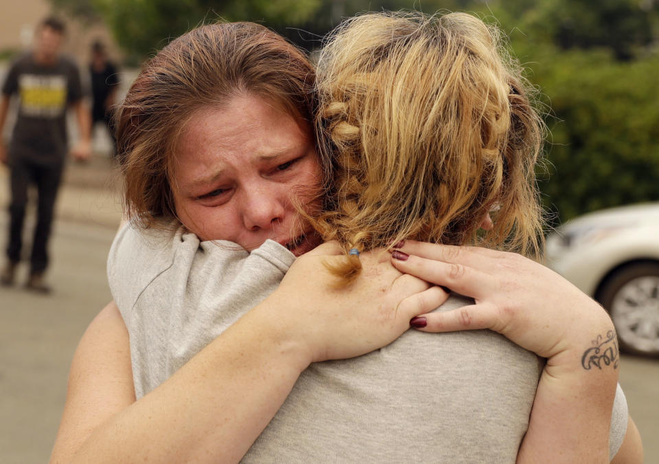 FILE - In this July 28, 2018, file photo, Carla Bledsoe, facing camera, hugs her sister Sherry outside of the sheriff's office after hearing news that Sherry's children James, 4, and Emily 5, and grandmother were killed in a wildfire in Redding, Calif. While California officials quickly determined an arsonist started the wildfire burning southeast of Los Angeles and that sparks from a vehicle produced the deadly wildfire in the city of Redding, causes for many of the state's worst blazes in the past decade remain a mystery. (AP Photo/Marcio Jose Sanchez, File)