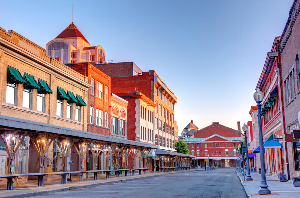 A quiet, empty street lined with storefronts and restaurants with awnings, under a clear sky, in an urban area