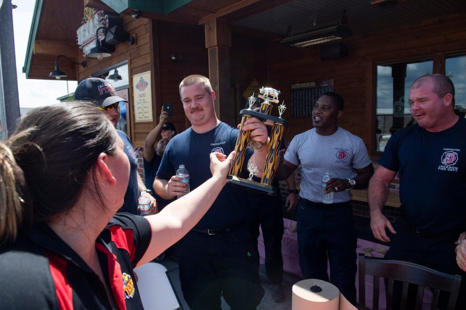 Texas Roadhouse employee Iris Barnes hands Hayden Towater a trophy after the firefighter team won during the Battle of the Badges Rib Eating Contest in which a team from the Jackson Fire Department went up against a team from the Jackson Police Department in a relay to see which team could eat the ribs the fastest at Texas Roadhouse on Monday, August 22, 2022, in Jackson, Tenn. The event was to promote the Dine to Donate fundraising night at Texas Roadhouse on Monday, August 29, where ten percent of the total food purchases will go towards the Carl Perkins Exchange Club.