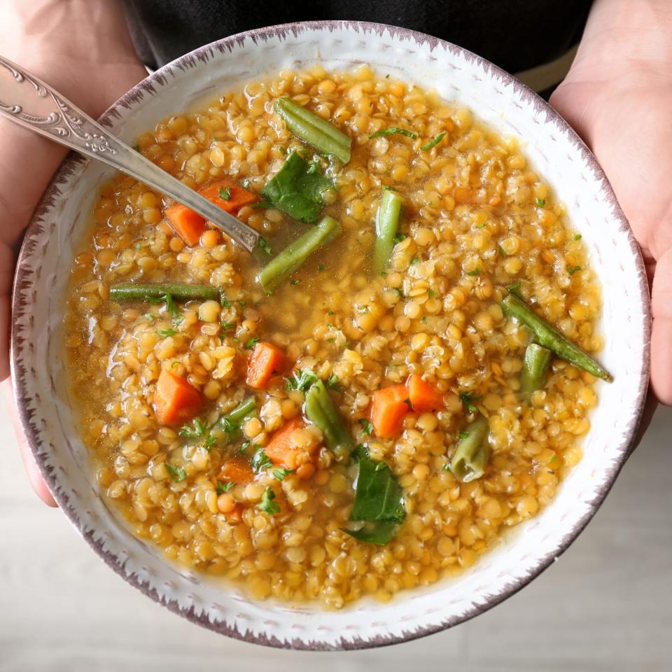 Young woman holding plate with tasty lentil dish, closeup