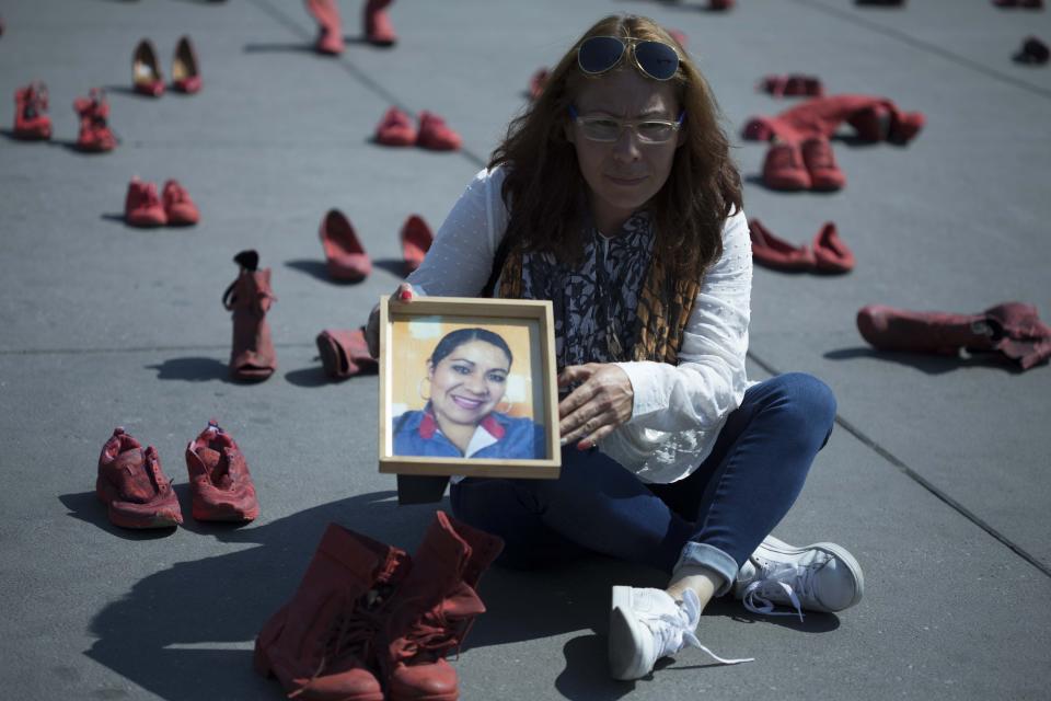 Elizabeth Machuca Campos holds the portrait of her sister Eugenia Machuca Campos amid women's red shoes placed in the Zocalo by people protesting violence against women in Mexico City, Saturday, Jan. 11, 2020. According to Elizabeth, her sister's ex-boyfriend is serving time in jail for her Oct. 2017 murder in the State of Mexico. (AP Photo/Christian Palma)