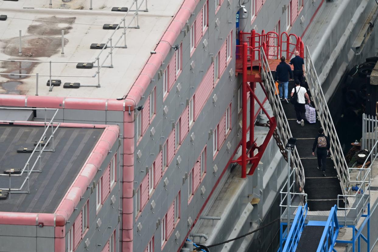 People carrying bags are seen walking up the gang-way into the the Bibby Stockholm accommodation barge, moored to the quayside at Portland Port in Portland, on the south-west coast of England on August 7, 2023. Britain on Monday began housing migrants on board a barge docked off the south-west English coast, in its latest controversial immigration policy that has drawn heavy criticism from locals and rights campaigners. (Photo by Ben Stansall / AFP) (Photo by BEN STANSALL/AFP via Getty Images)