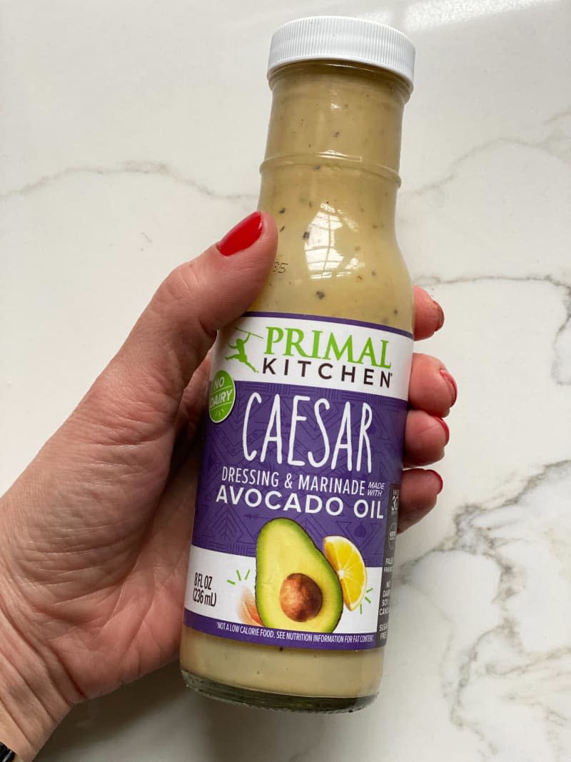 Someone holding a bottle of Primal Kitchen Caesar dressing & marinade