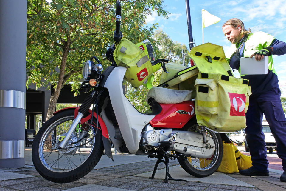 Australia Post courier loading postal packages into a delivery scooter. Source: Getty Images