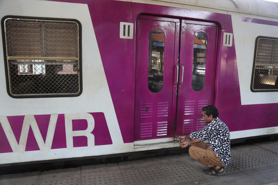 A railway employee locks the door of a suburban train in Mumbai, India, Monday, March. 23, 2020. As India expanded its virus-containment measures and halted its lifeblood - the local and national train network, the federal government warned Monday of strict legal action for those who flout the rules. For most people, the new coronavirus causes only mild or moderate symptoms. For some it can cause more severe illness. (AP Photo/Rafiq Maqbool)