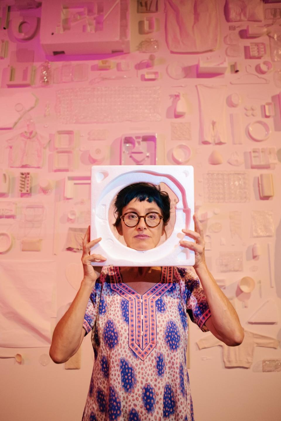 Pipilotti Rist holds a piece of styrofoam as a frame around her head in front of a wall installation