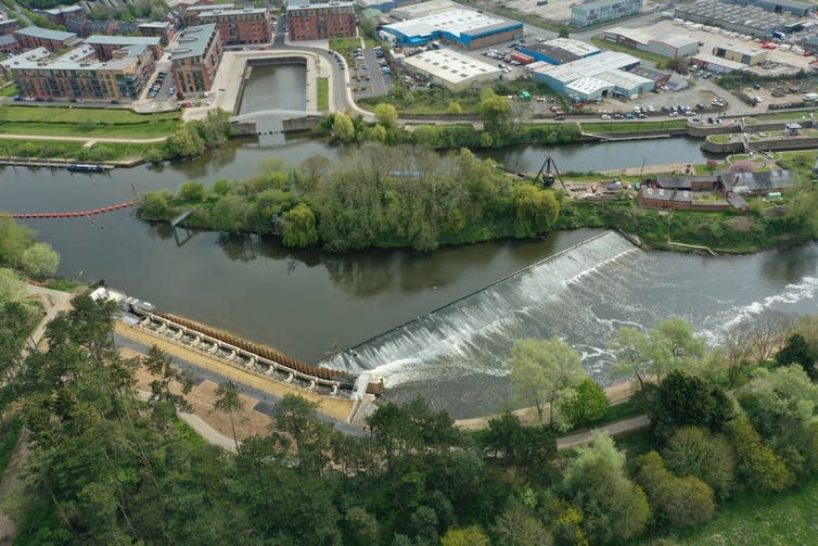 An aerial view of a river with a weir and a stone passage bypassing it.