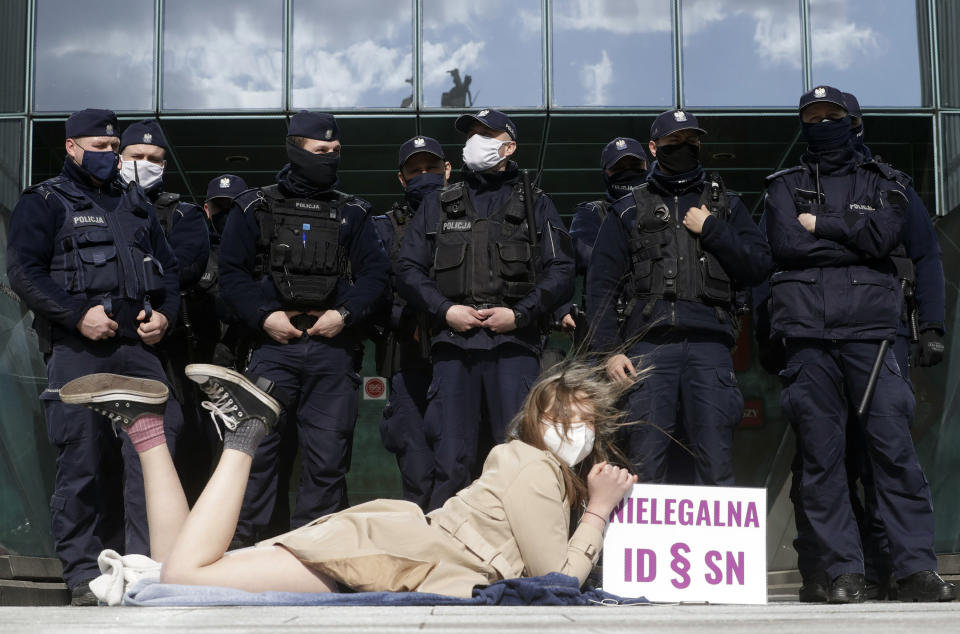 Policemen guard Poland's Supreme Court as a protester lies on the pavement in Warsaw, Poland, on Thursday, April 22, 2021. A disputed disciplinary body within Poland's Supreme Court is examining a motion that could result in the arrest of a judge who has become a symbol of the fight for an independent judiciary. The Disciplinary Chamber is due to decide whether to force Judge Igor Tuleya to answer to prosecutors about charges related to a ruling that went against the interests of the ruling Law and Justice party. Sign read in Polish "Illegal ID - SN”, where ID means Disciplinary Chamber and SN means Supreme Court. (AP Photo/Czarek Sokolowski)