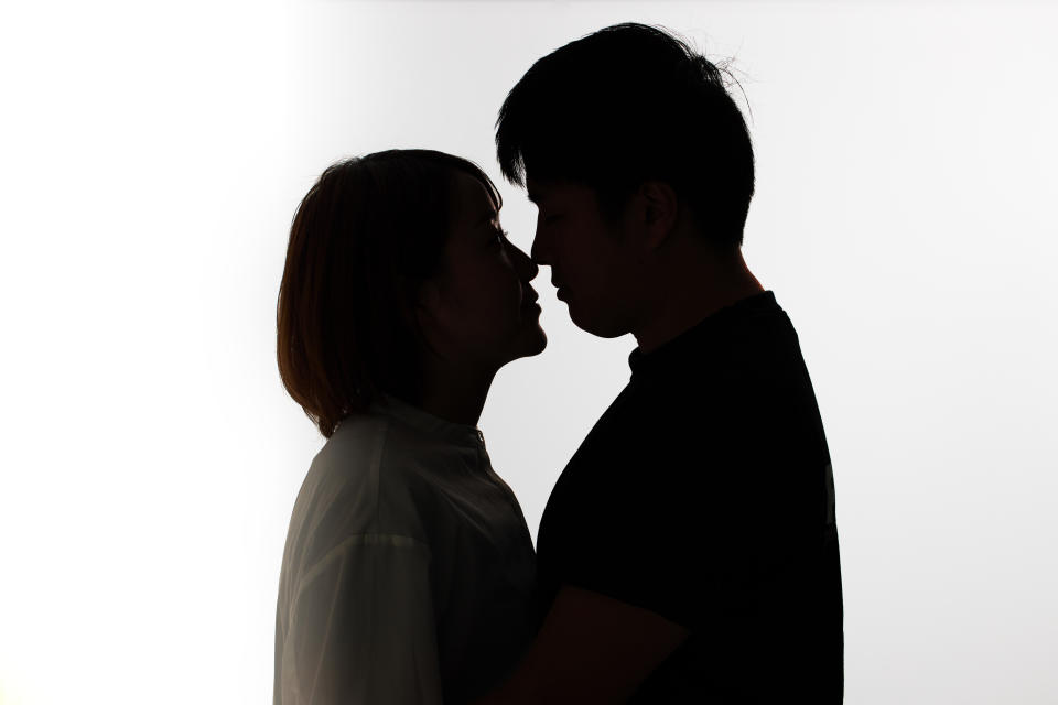 A silhouetted couple faces each other, seemingly about to kiss, against a plain background, conveying a romantic moment. Names unidentified