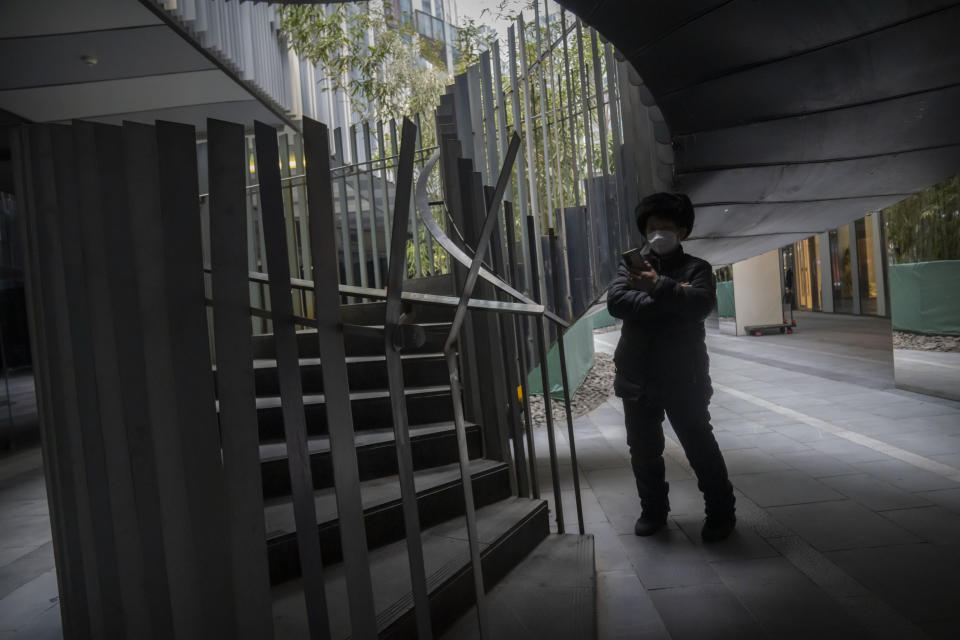 A woman wearing a face mask looks at her smartphone at a shopping and office complex in Beijing, Wednesday, Jan. 11, 2023. Japan and South Korea on Wednesday defended their border restrictions on travelers from China, with Tokyo criticizing China's move to suspend issuing new visas in both countries as a step unrelated to virus measures. (AP Photo/Mark Schiefelbein)