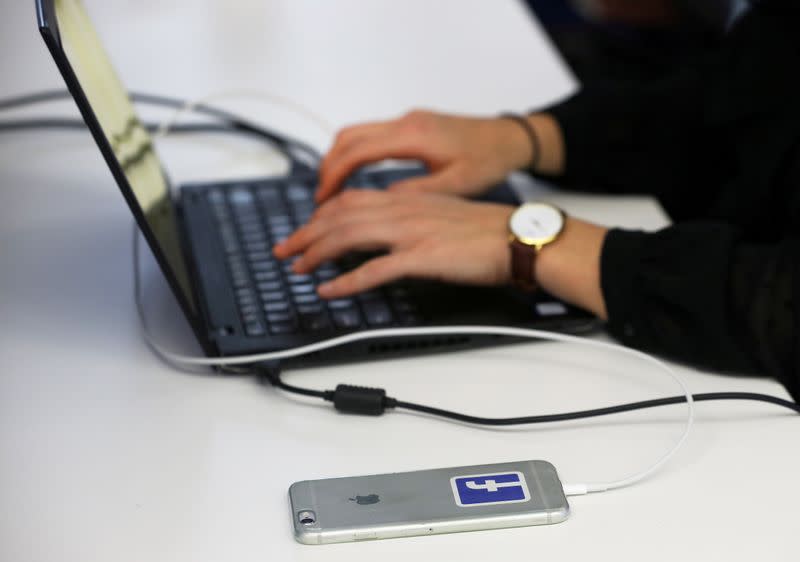 FILE PHOTO: Facebook sticker is seen on a mobile phone while an employee works at the Facebook's elections operation centre in Dublin