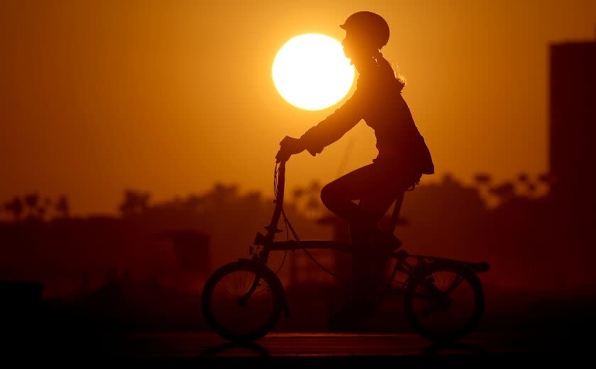 LONG BEACH, CALIF. - AUG. 11, 2022.. The sun sets as a woman pedals down the bike path in Long Beach. (Luis Sinco / Los Angeles Timesd)