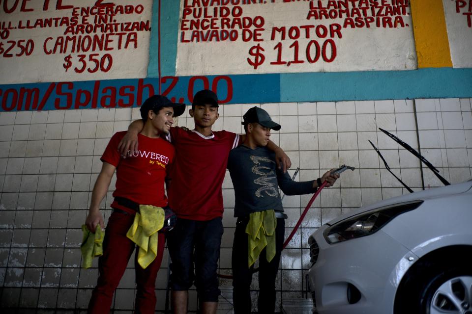 In this Nov. 27, 2018 photo, migrants Nelson Landaverde, left, Angel Lemus, center, and Erick Canales, who traveled with a caravan of Central American migrants, pose for a photo at their new job as car washers, in Tijuana, Mexico. “Here you make a little money, I can take something to eat to my baby,” said Landaverde, a 21-year-old from Copan, Honduras. Landaverde and his pregnant wife have already put their names on an informal list to apply for asylum in the U.S., but in the meantime he wants to earn money to make their lives a little more comfortable in Tijuana. (AP Photo/Ramon Espinosa)