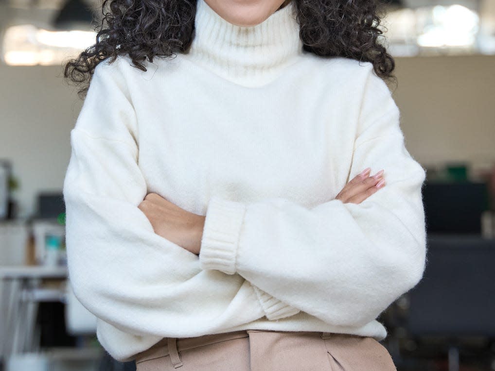 woman wearing a cream sweater and brown trousers in an office