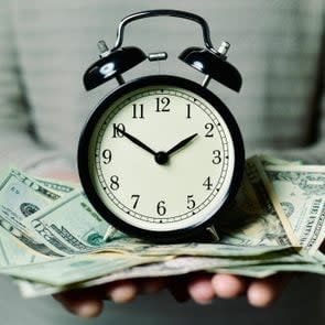 close up of a person holding an alarm clock sitting on US bills in the person's hands