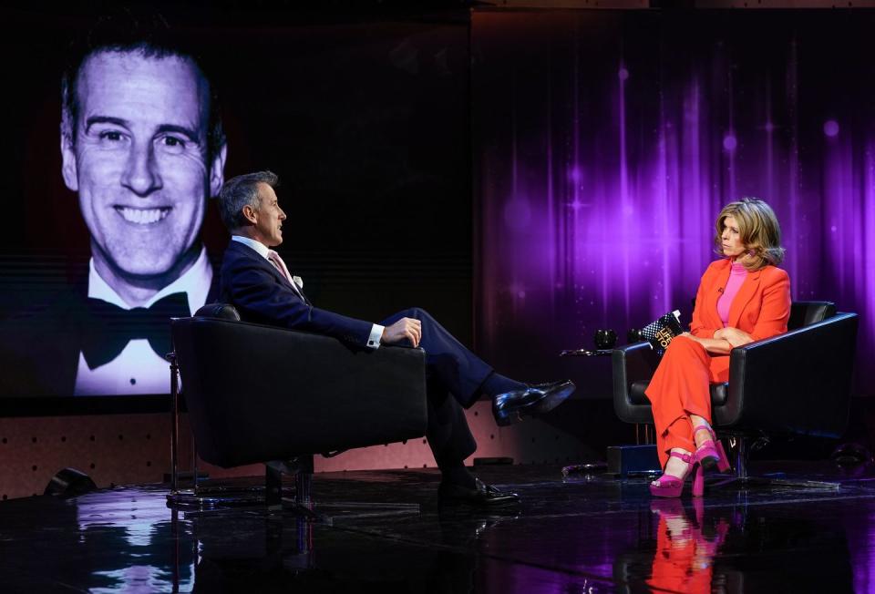 anton du beke and kate garraway sit opposite each other in a tv studio with solemn facial expressions, he wears and black suit and she wears a red suit