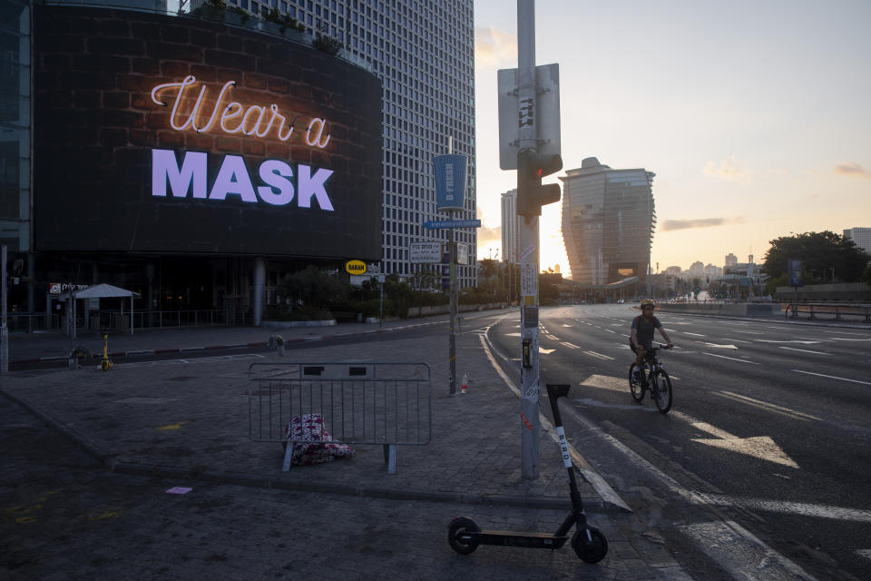 A man rides a bicycle next to a billboard calling people to wear masks, on empty road following new restrictions in the three-week nationwide lockdown, in Tel Aviv, Israel, Saturday, Sept. 26, 2020. (AP Photo/Oded Balilty)