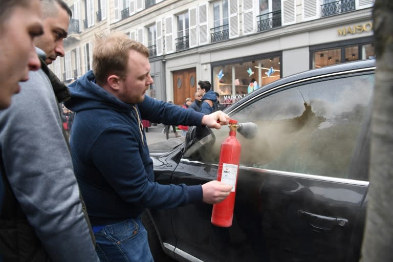 A man tries to extinguish a fire inside a car on the sidelines of a demonstration in Paris on Thursday