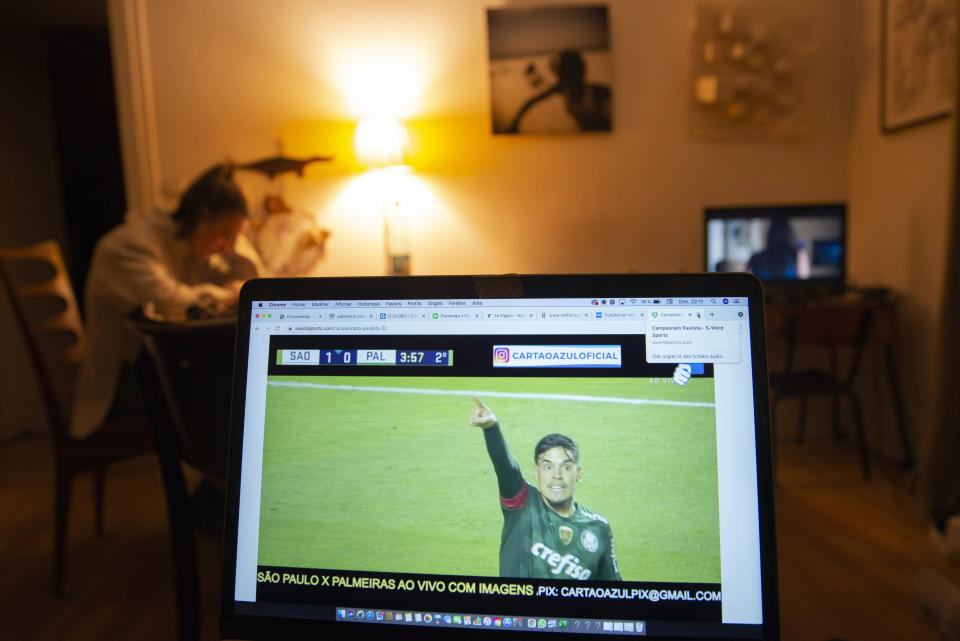 Anais Bulcao, 17, does her homework in the sitting and dining room of her family's apartment in Montmartre on May 23, 2021, while her Brazil-born father watches Palmeiras beat Sao Paolo 2-0 in the Sao Paolo state soccer championship. With roots in both France and Brazil, the family feels fortunate to have weathered the pandemic in Paris. "It would have been a lot more complicated in Brazil," says Anais father, Joao Luiz Bulcao. (AP Photo/Joao Luiz Bulcao)