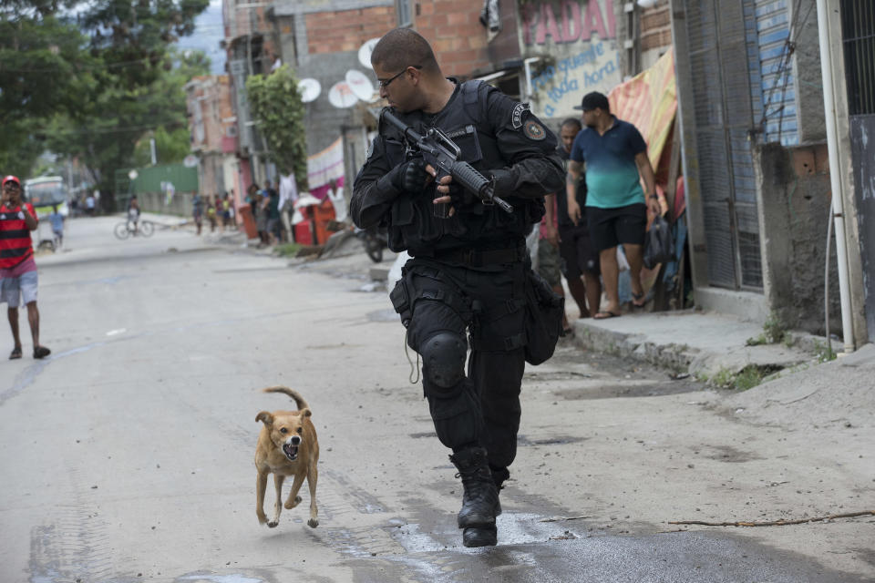 In this Wednesday, March 26, 2014 photo, a Special Police Operations Battalion (BOPE) officer is chased by a barking dog during an operation in the Mare slum complex, ahead of its "pacification," in Rio de Janeiro, Brazil. Elite federal police and army troops will be sent to the city to help quell a wave of violence in so-called "pacified" slums. (AP Photo/Silvia Izquierdo)