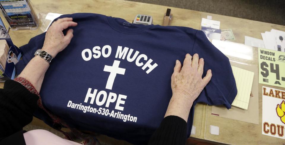 A customer rests her hands on a tee-shirt for sale at a sporting goods store with proceeds to be directed to victims of a deadly landslide Friday, March 28, 2014, in Arlington, Wash. The death toll from the mudslide in nearby Oso, Wash., is expected to rise considerably within the next two days as the Snohomish County Medical Examiner's Office catches up with the recovery effort, Snohomish County District 21 Fire Chief Travis Hots said Thursday. (AP Photo/Elaine Thompson)