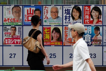 People walk past election campaign posters outside a voting station during Japan's upper house election in Tokyo