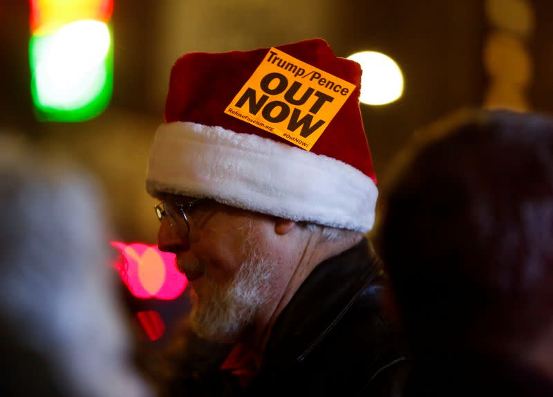 A man in a Santa hat wears a bright sticker during a rally to support the impeachment and removal of President Trump in Seattle