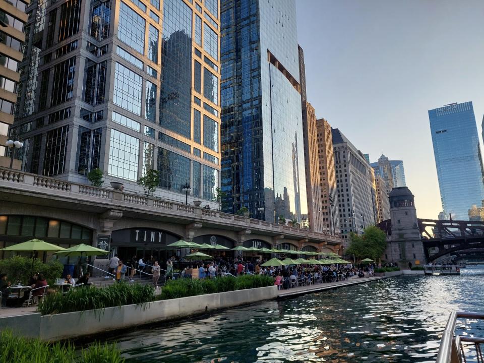 A photo showing the river in Chicago with a riverside path full of tables of customers eating and drinking