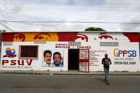 A man walks past a campaign office of Venezuela's United Socialist Party (PSUV) with a billboard with pictures of Venezuela's President Nicolas Maduro and late Venezuelan President Hugo Chavez, in Sabaneta, in the state of Barinas, November 19, 2015. REUTERS/Marco Bello.