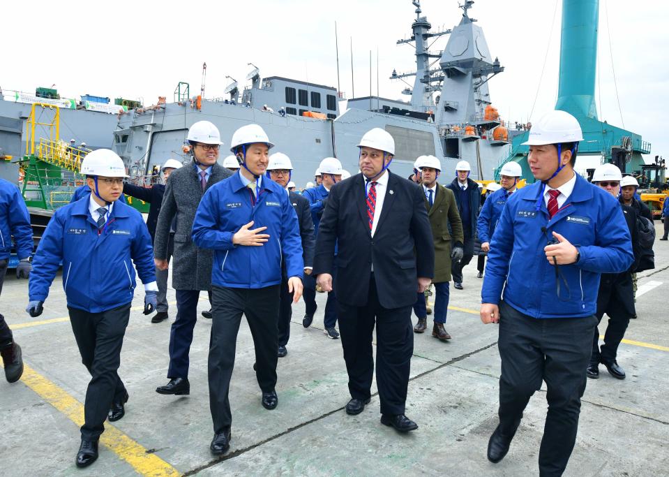 Carlo Del Toro in the middle of a group of men in a shipyard, all wearing white hard hats.