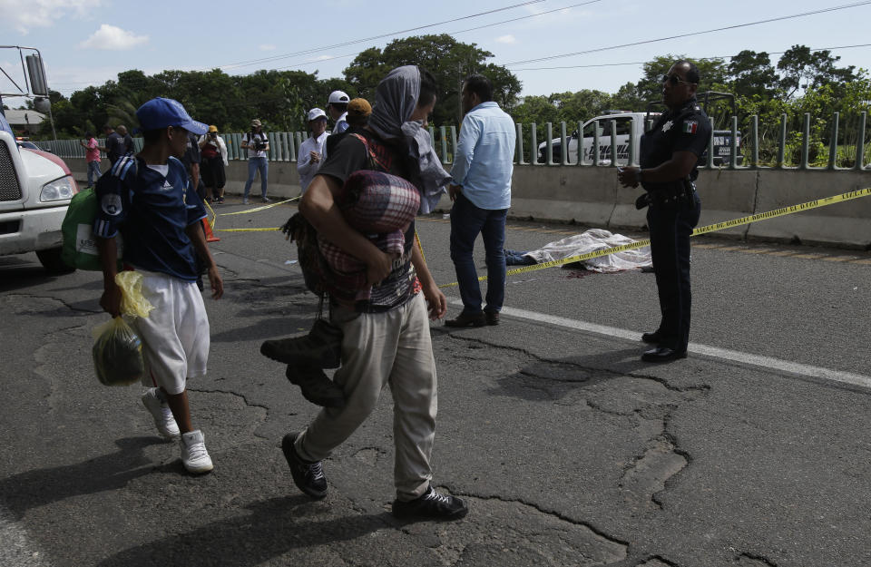 A Central American migrant who fell from the back of a moving vehicle and died, lies on a highway behind police as other migrants from the same caravan walk on the outskirts of Tapachula, Mexico, Monday, Oct. 22, 2018. Motorists in pickups and other vehicles have been offering the Central American migrants rides, often in overloaded truck beds, as the group of about 7,000 people heads to the U.S. border. (AP Photo/Moises Castillo)