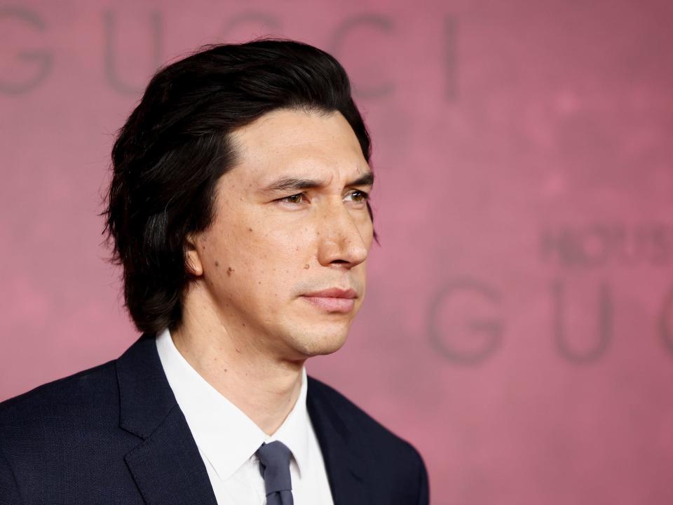 adam driver in a suit in front of a pink wall