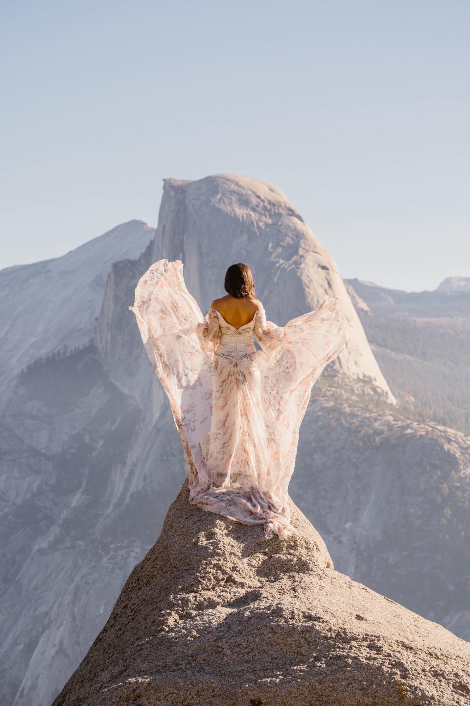 A bride stands on a cliff and her wedding dress flies around her.