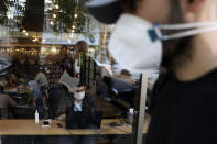 A man wearing a protective face mask to help prevent the spread of the coronavirus works on his computer in a cafe as another one walks past, in Tehran, Iran, Sunday, Sept. 20, 2020. Iran's president dismissed U.S. efforts to restore all U.N. sanctions on the country as mounting economic pressure from Washington pushed the local currency down to its lowest level ever on Sunday. (AP Photo/Vahid Salemi)