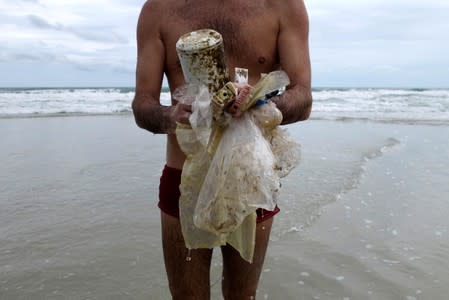 FILE PHOTO: Tourist collects plastic items washed up by the sea at the Ao Phrao Beach, on the island of Ko Samet