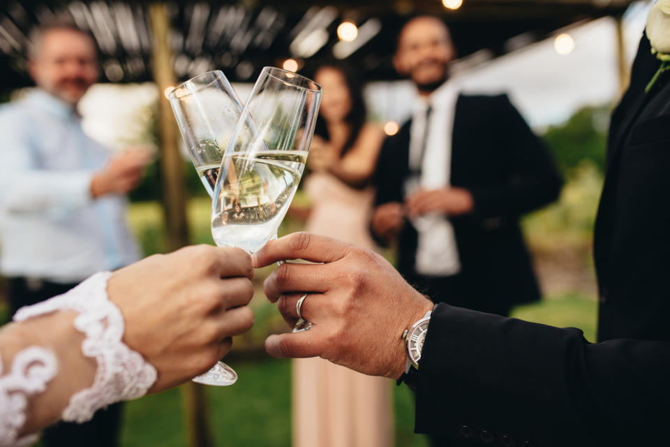 Two people at a wedding hold their champagne glasses together