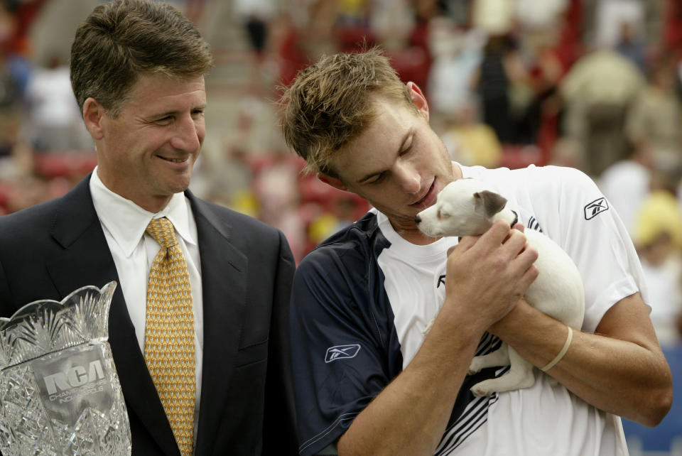 Andy Roddick of the USA holds Chipper, one of the RCA dogs, after defeating Paradorn Srichaphan of Thailand during the finals of the 2003 RCA Championships while tournament Robert MacGill holds the trophy at the Indianapolis Tennis Center July 27, 2003 in Indianapolis, Indiana. Roddick won 7-6 (2), 6-4.