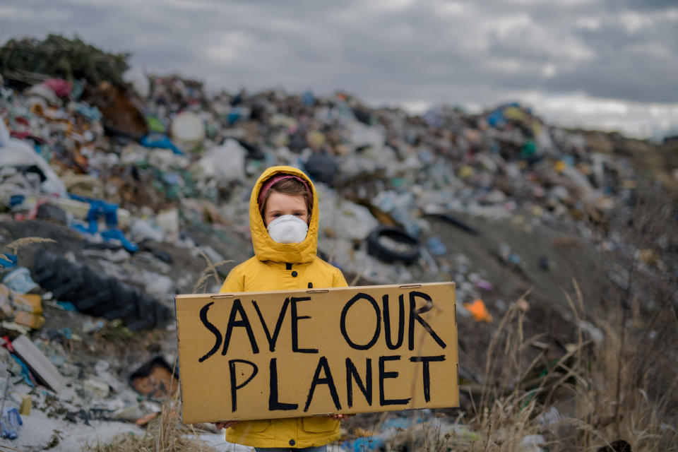 A child in a landfill holding a sign that says, "Save Our Planet"