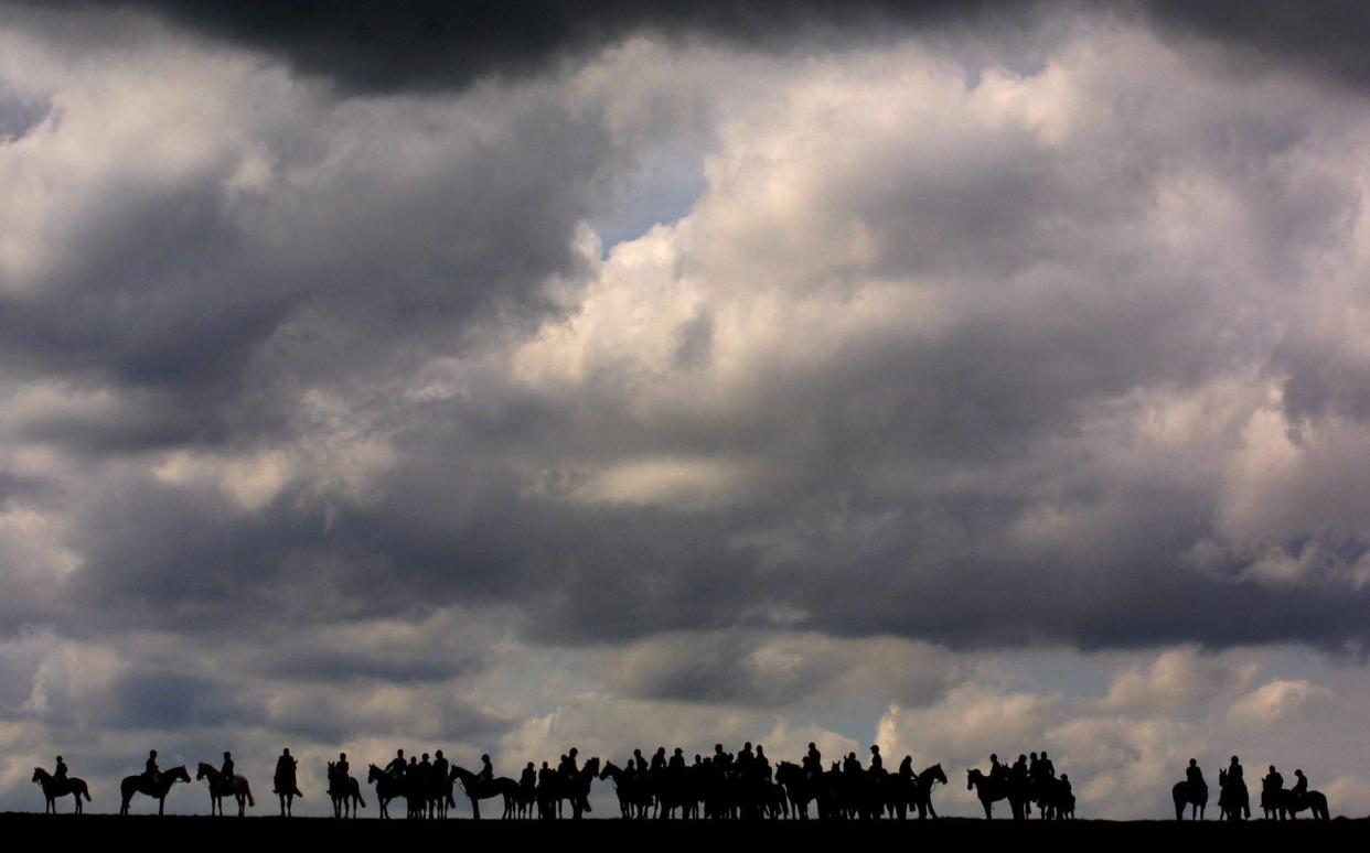 A fox hunt seen in silhouette on the horizon under a lowering sky