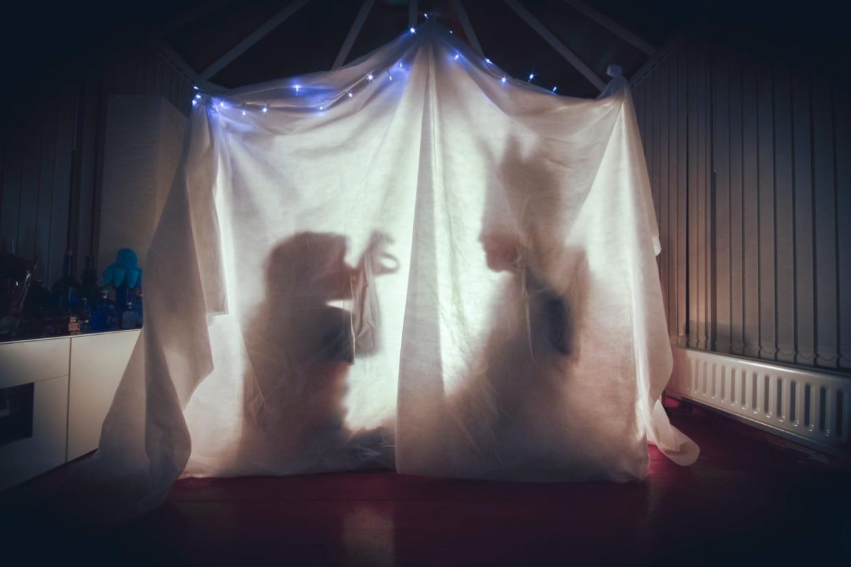 Silhouettes of child and adult telling stories in a homemade fort