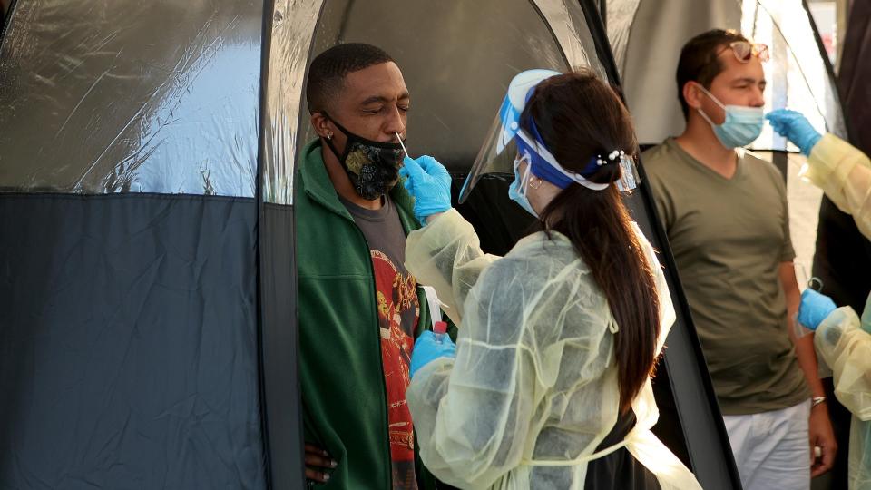 A female medical worker administering a COVID-19 test to a man in a tent