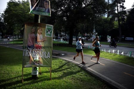 Women run in front of a campaign sign for the National Unity of Hope (UNE), ahead of the second round run-off vote, in Guatemala City